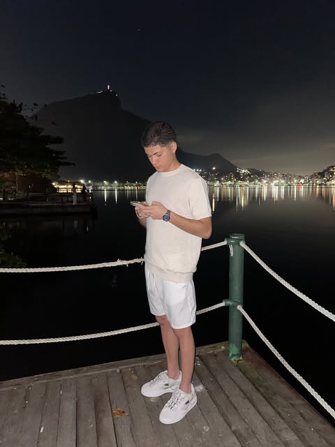 Cauê Alves de pé num deque à noite, com a Lagoa Rodrigo de Freitas e o Cristo Redentor ao fundo